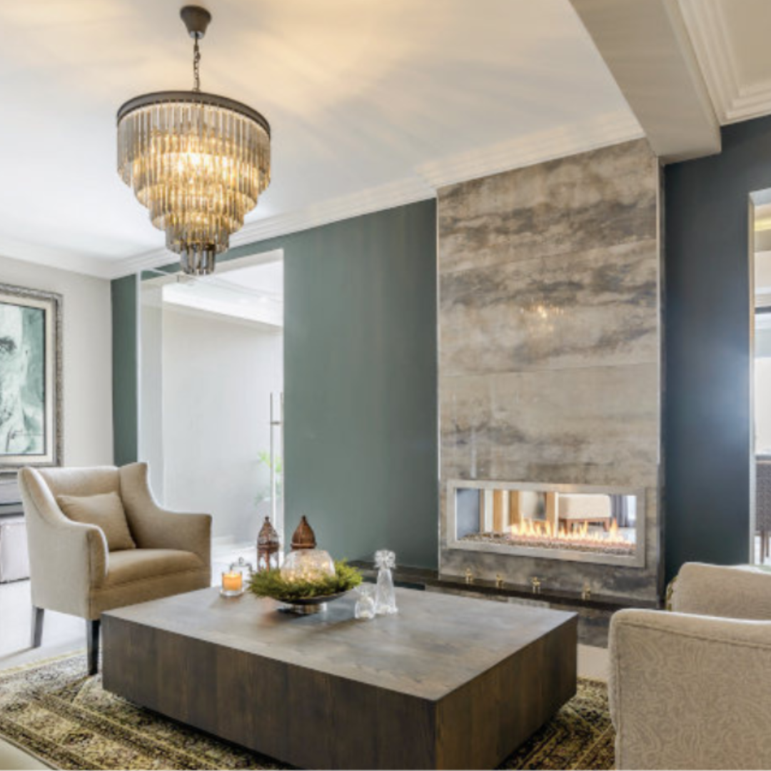 A modern living room featuring a double-sided fireplace with a marble surround, Insert visible with a warm fire glow, seating arrangement, and a decorative chandelier above.