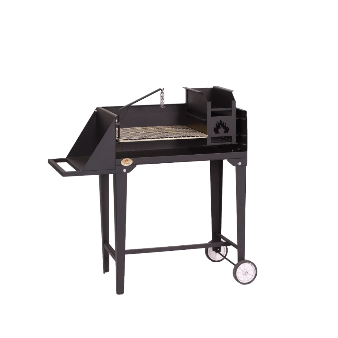 A black trolley braai grill with a stainless steel grid, integrated ash pan, and poker potjie hook, set on a frame with wheels and a work surface.