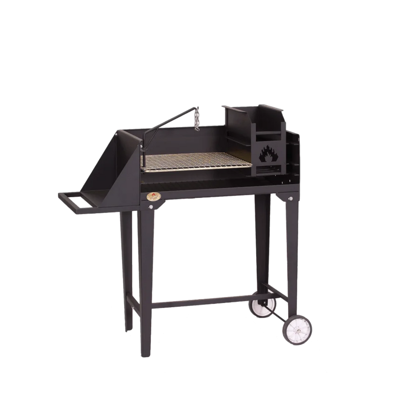 A black trolley braai grill with a stainless steel grid, integrated ash pan, and poker potjie hook, set on a frame with wheels and a work surface.