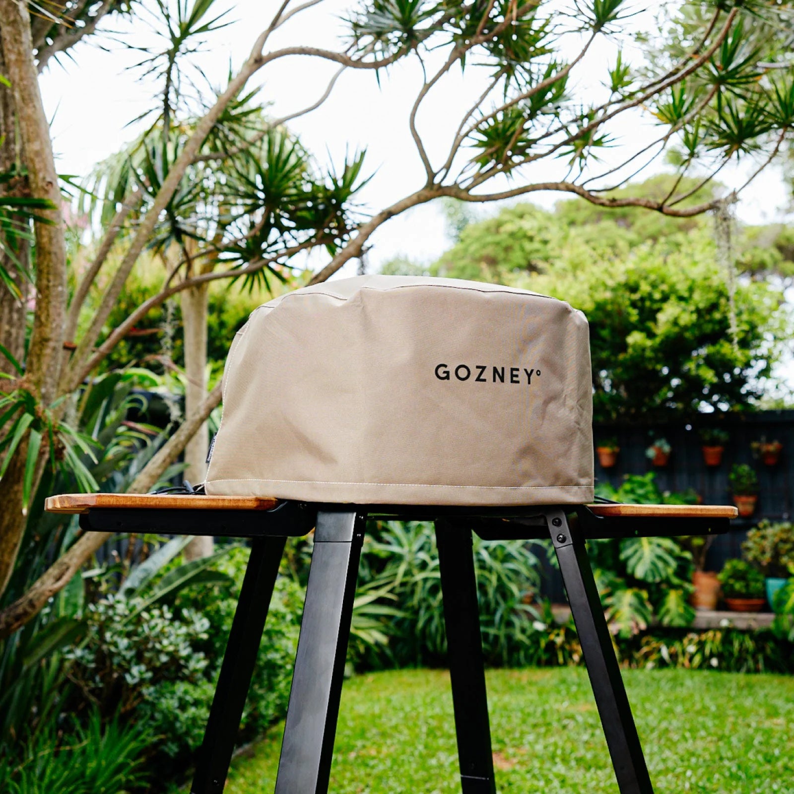 Beige Gozney grill cover on a stand in a garden setting
