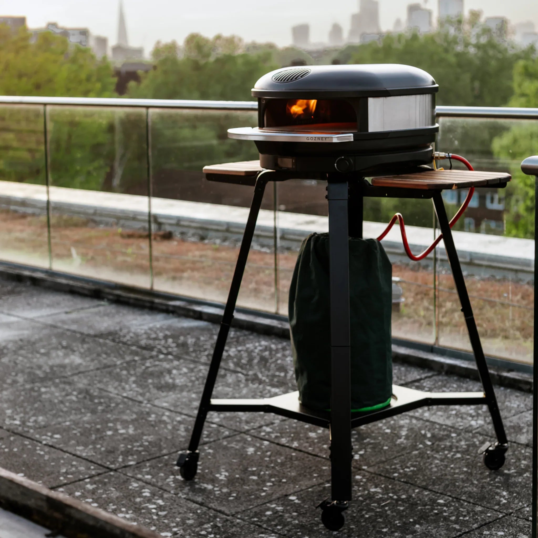 Portable pizza oven on a stand outdoors with a cityscape background