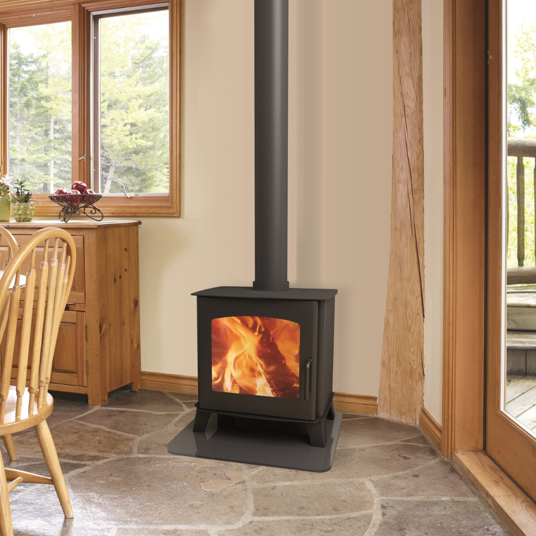 A black freestanding wood stove with a visible fire compartment, situated in a room with stone flooring and wooden furniture.