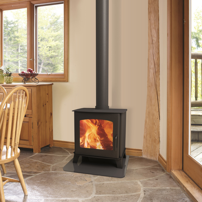 A black freestanding wood stove with a visible fire compartment, situated in a room with stone flooring and wooden furniture.