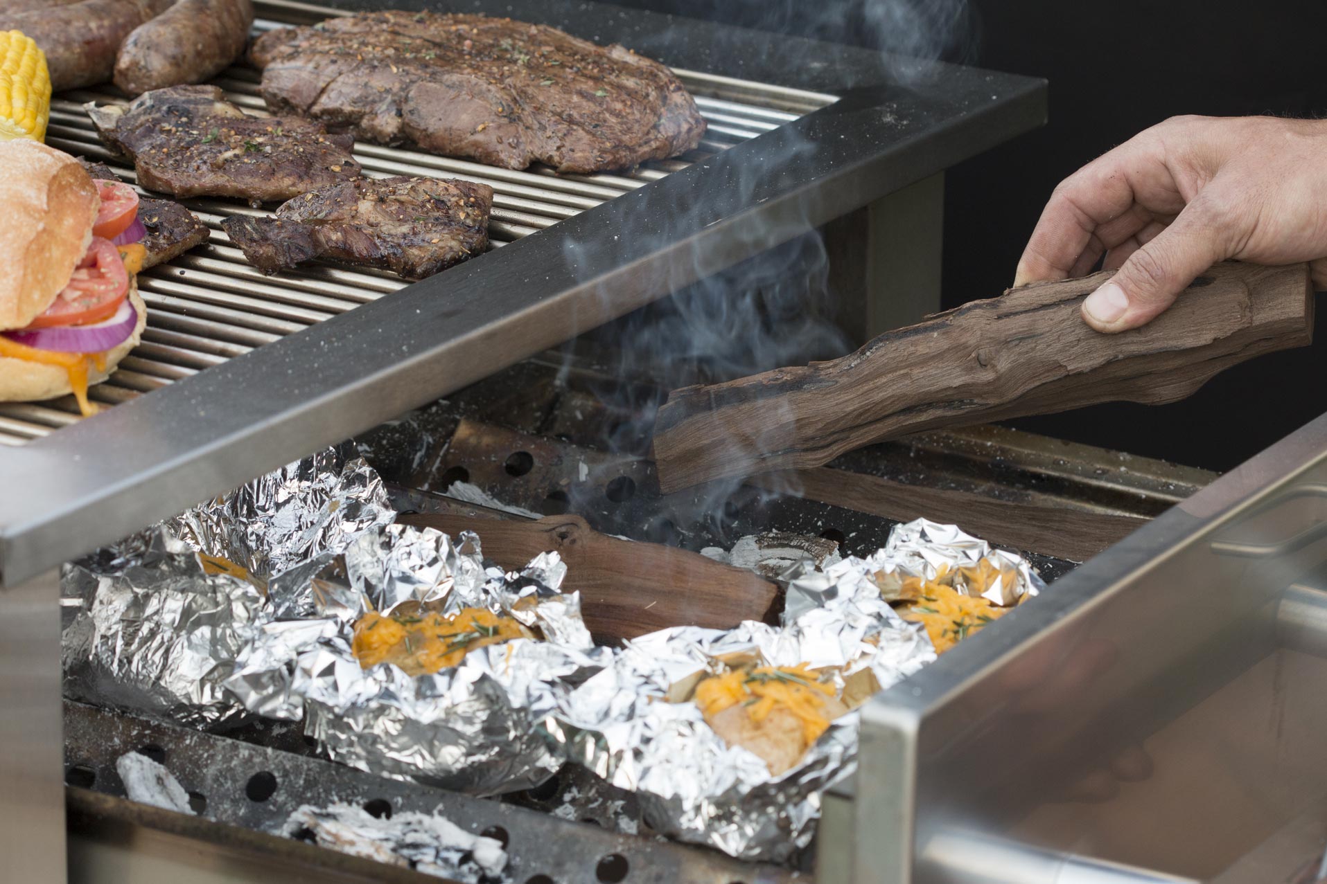 Hybrid gas and wood braai with ember drawer, potatoes roasting, outdoor lifestyle.