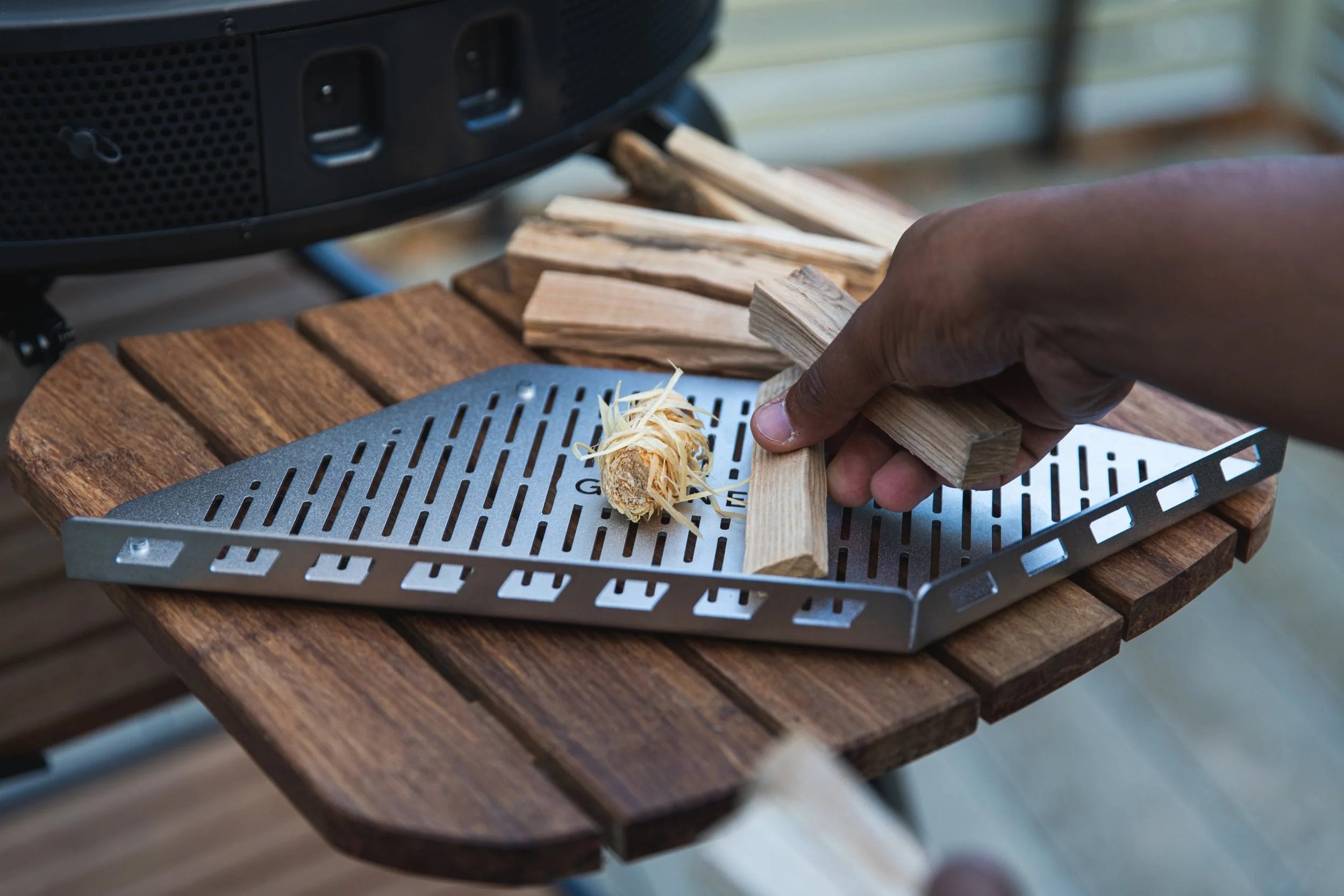 Person placing wood chips on a grill with a wooden surface
