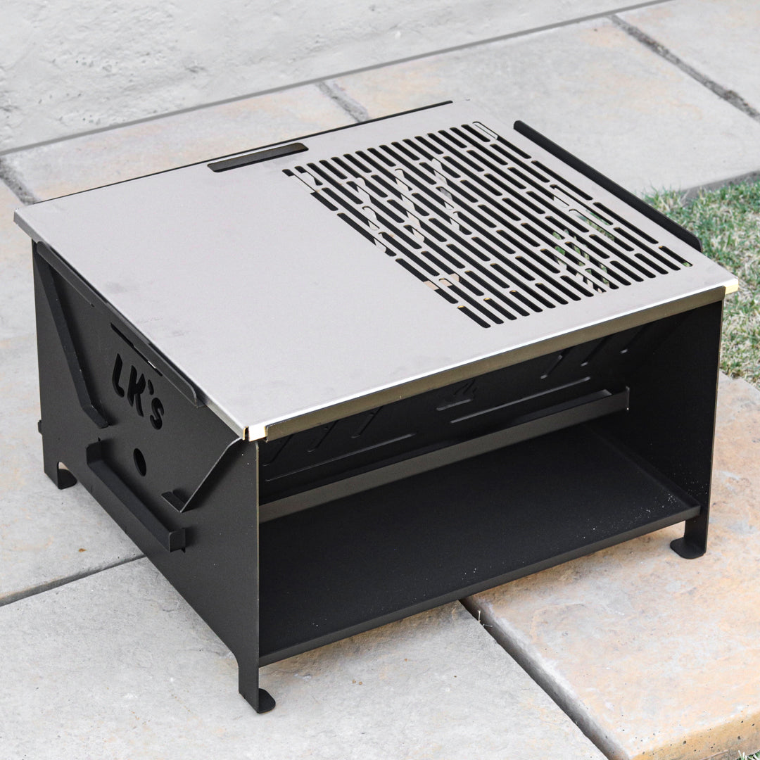 A black metal fire pit braai with a stainless steel grid and sides, designed for outdoor cooking and heating.