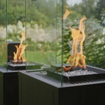 Kratki Patio M outdoor gas heater in garden setting with glass enclosure.