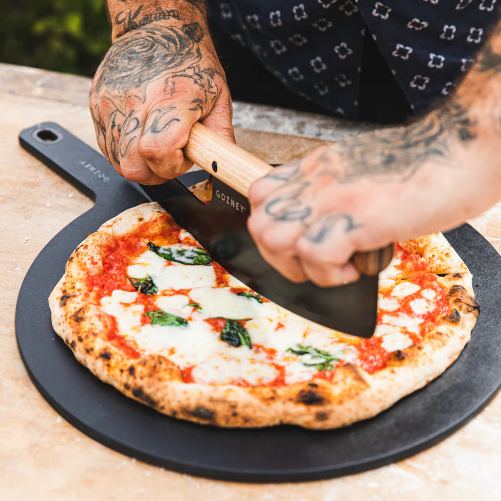 Person cutting a pizza with a spatula on a wooden surface