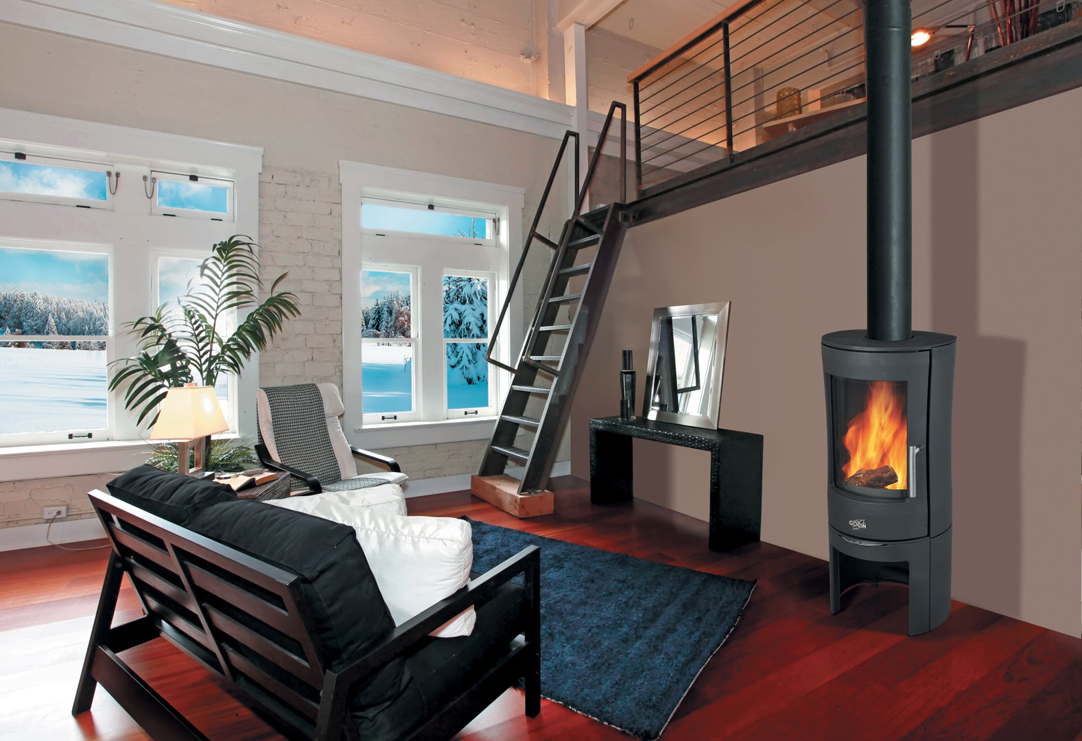 A modern freestanding black fireplace with visible flames, located in a spacious room with a staircase and a window with a view of a forest.
