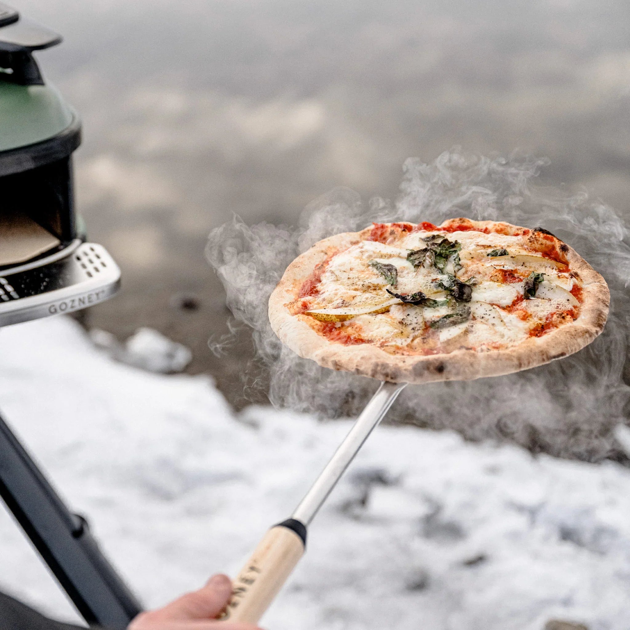 Person holding a pizza over a GoPro camera in a snowy outdoor setting
