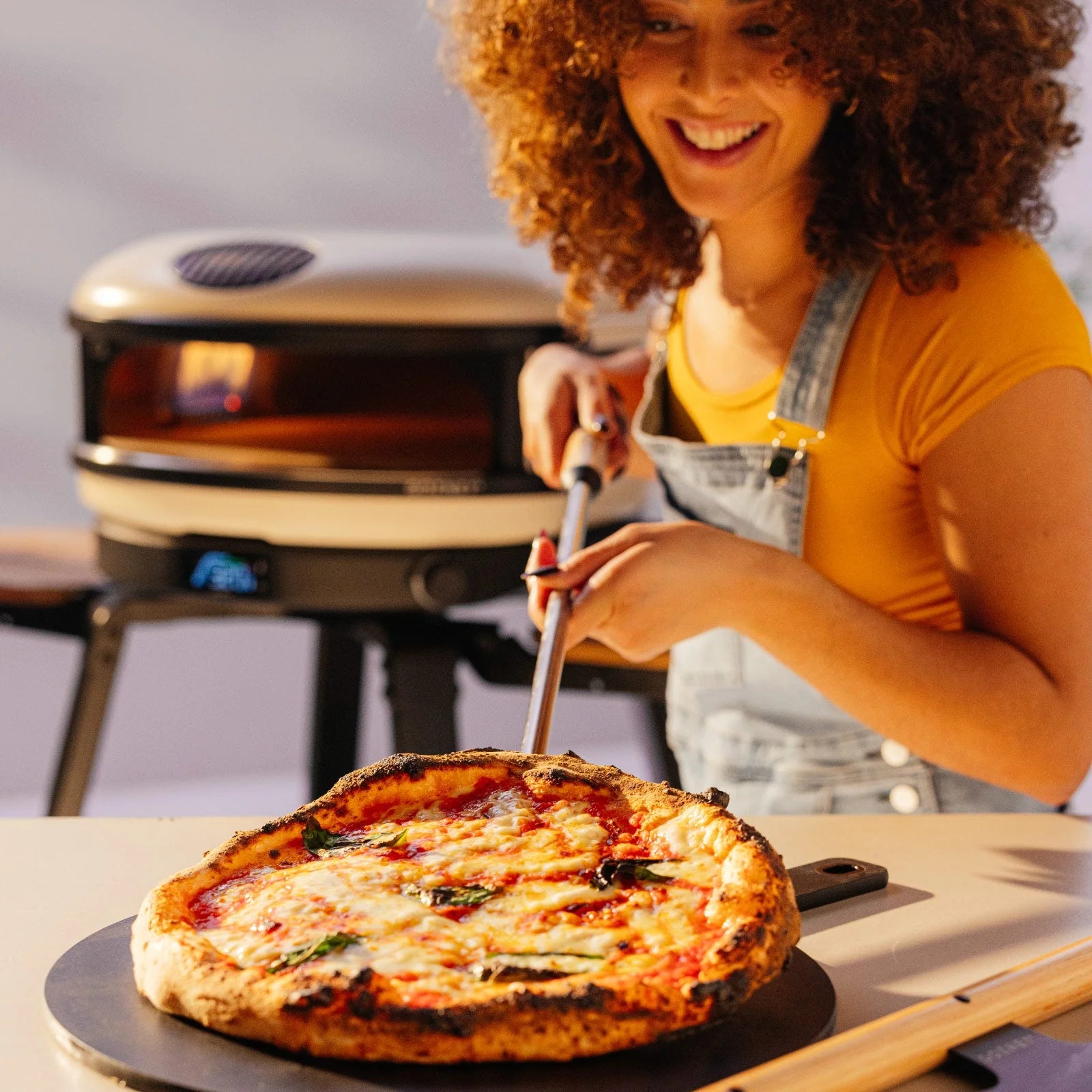 Woman with a pizza in front of an outdoor pizza oven