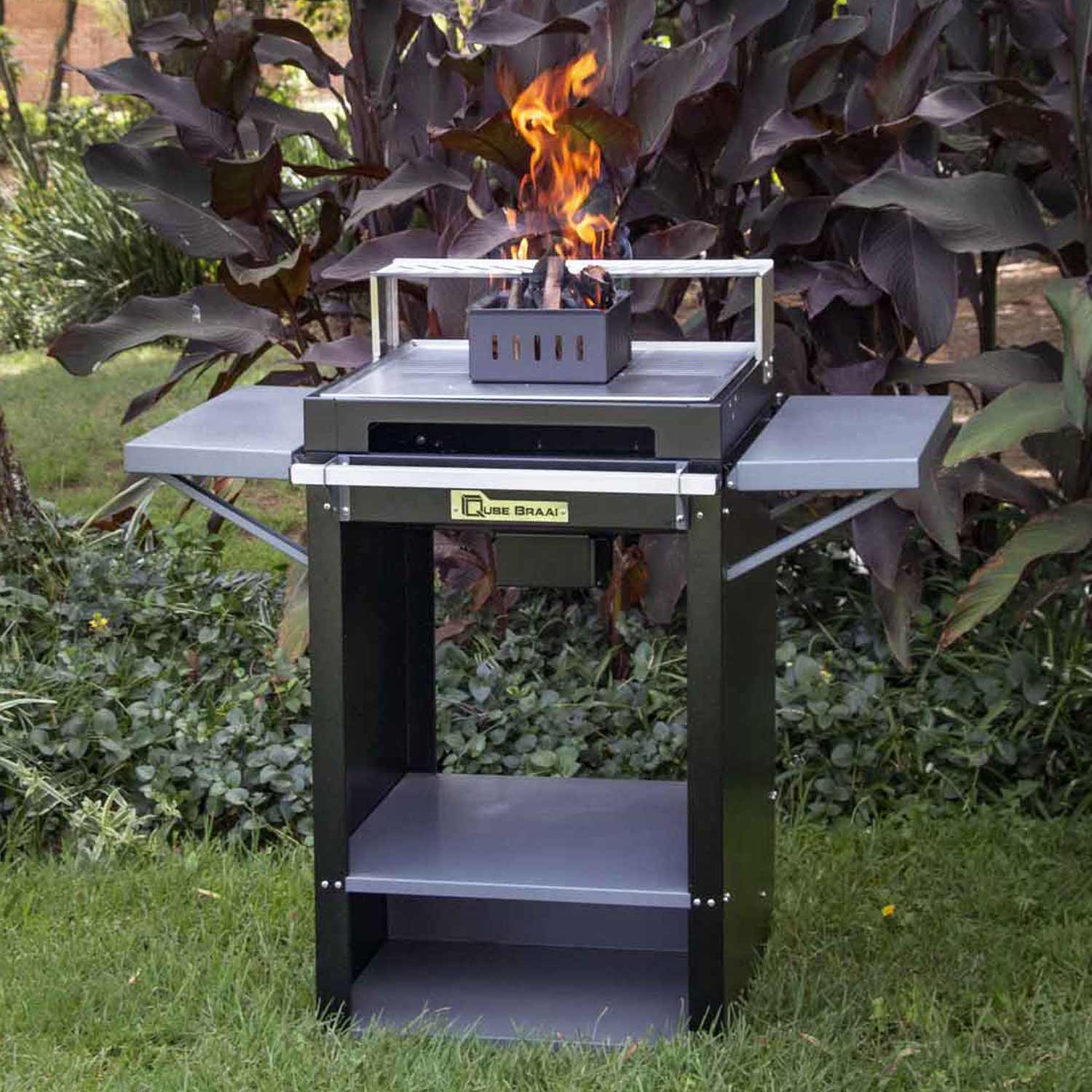 Outdoor grill with flames on a grassy area with plants in the background