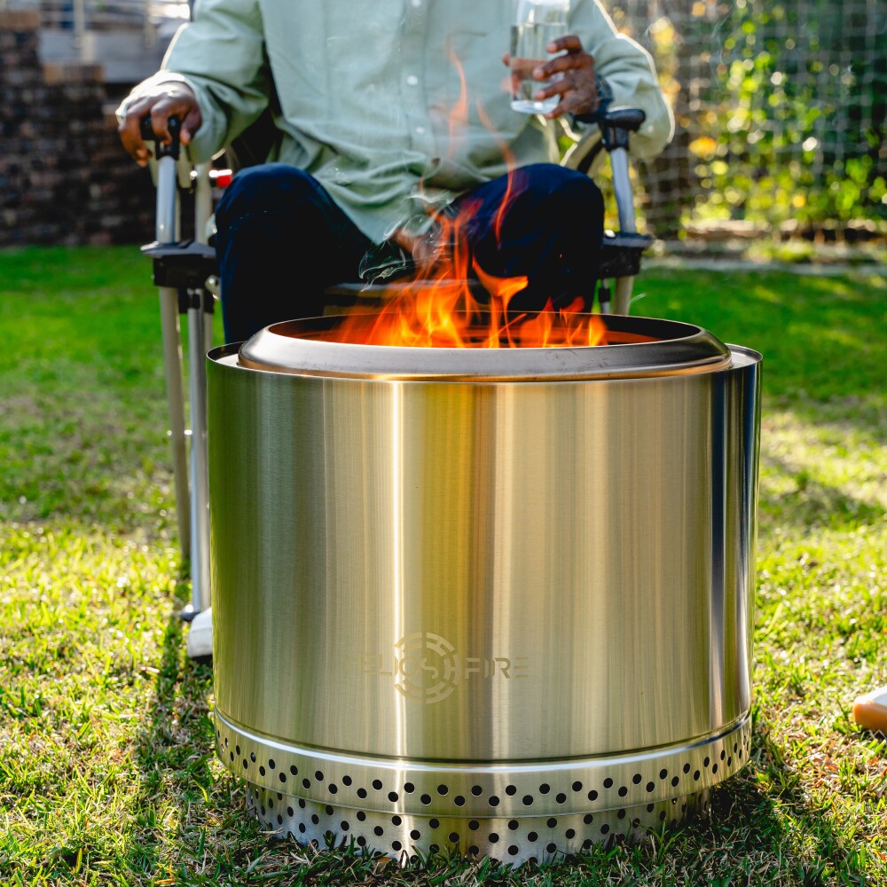 Stainless steel fire pit with flames on a grassy outdoor area