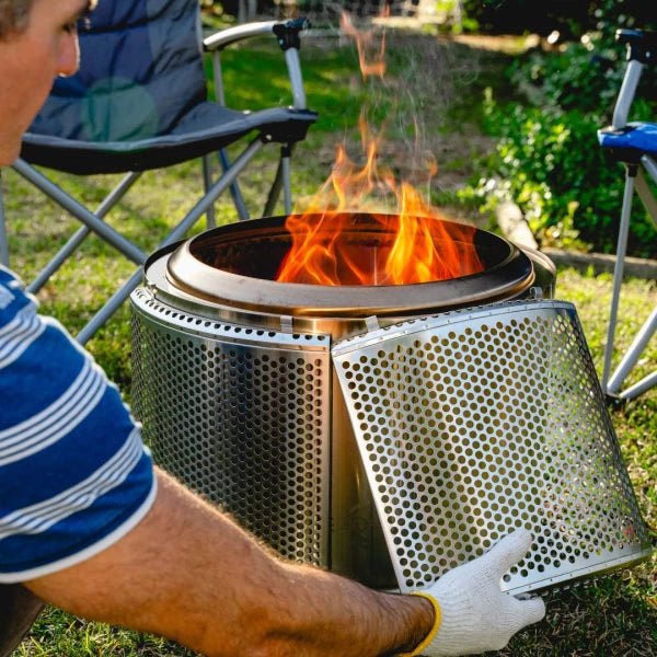 Person holding a metal fire pit with flames outdoors