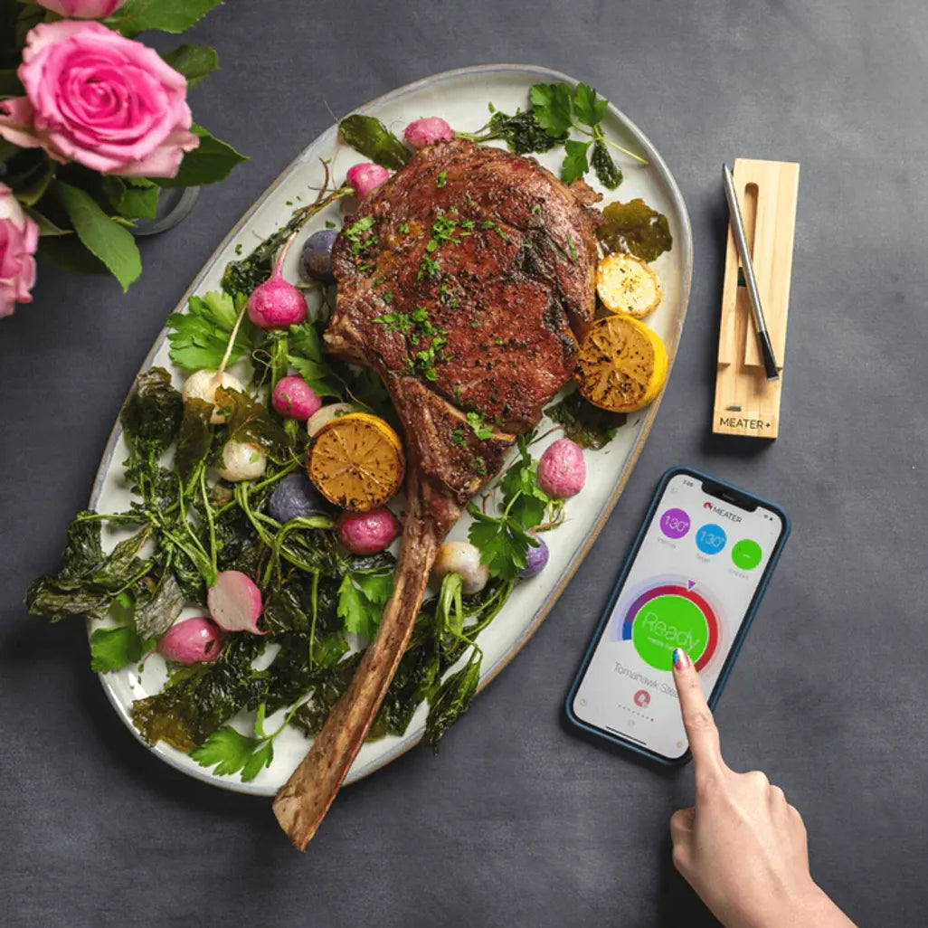 Steak on a plate with vegetables, pink roses, and a smartphone app on a dark surface